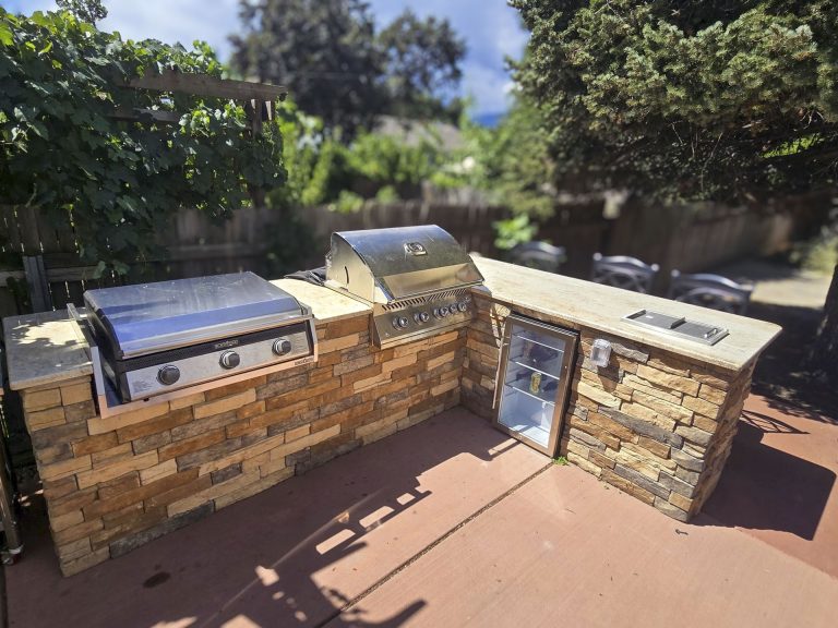 Outdoor brick kitchen with built-in grill, cooktop, and storage cabinets in a residential backyard setting