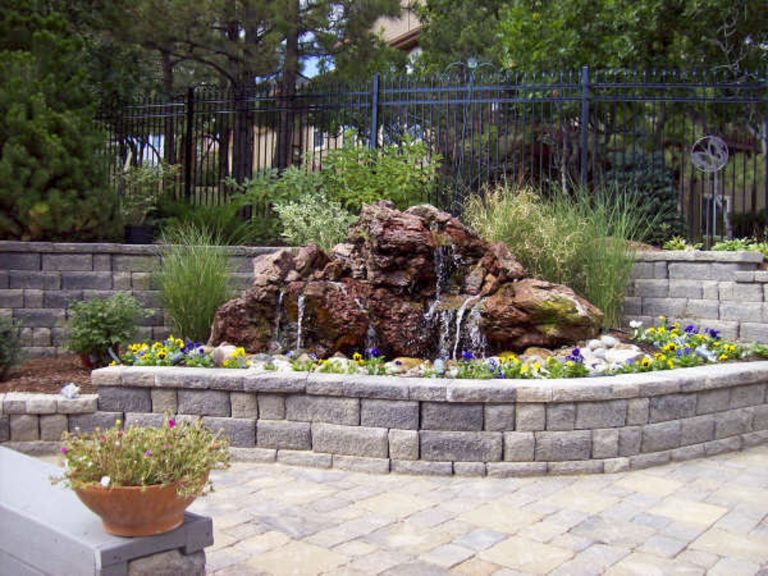 Circular stone planter bed with red rocks, ornamental grasses, and succulents in a residential landscape design