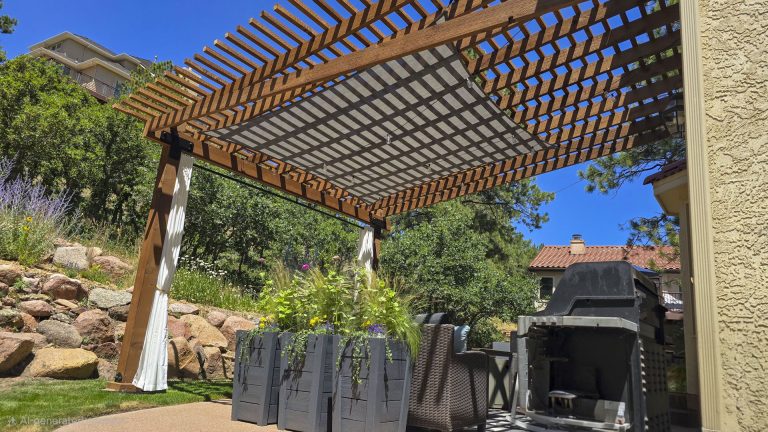 Wooden pergola with lattice roof over patio seating area with landscaping and stone wall