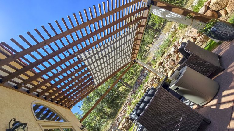 Wooden pergola with lattice roof creating dappled shade over a patio with potted plants and seating area