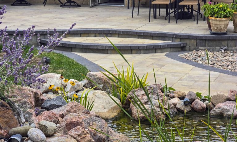 Modern patio with decorative rocks, ornamental grasses, and purple flowers along a curved stone pathway