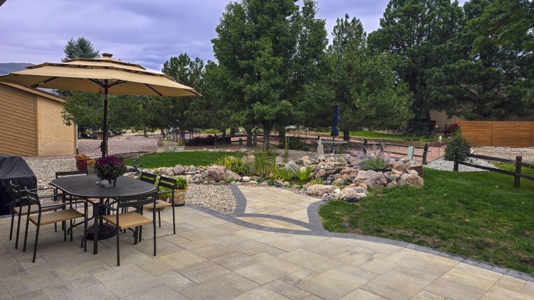 Residential backyard patio with umbrella, seating, flowering garden beds, and landscaping