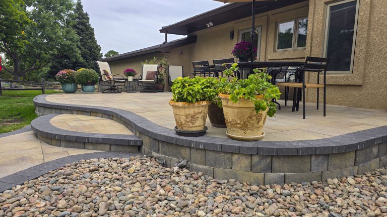 Modern patio with curved stone wall, gravel border, potted plants, and home exterior with deck in background