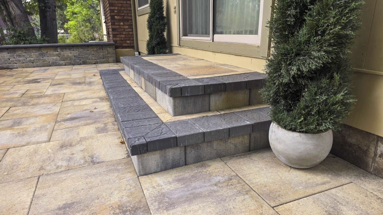 Outdoor patio with stone pavers, built-in bench seating, and potted plant against house exterior