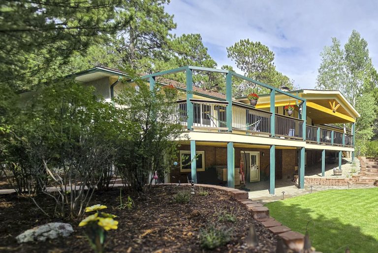 Modern two-story yellow house with white trim surrounded by green trees and manicured lawn