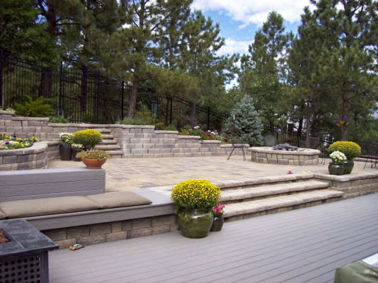 Multi-level composite deck with stone steps, planters, and pine trees in background