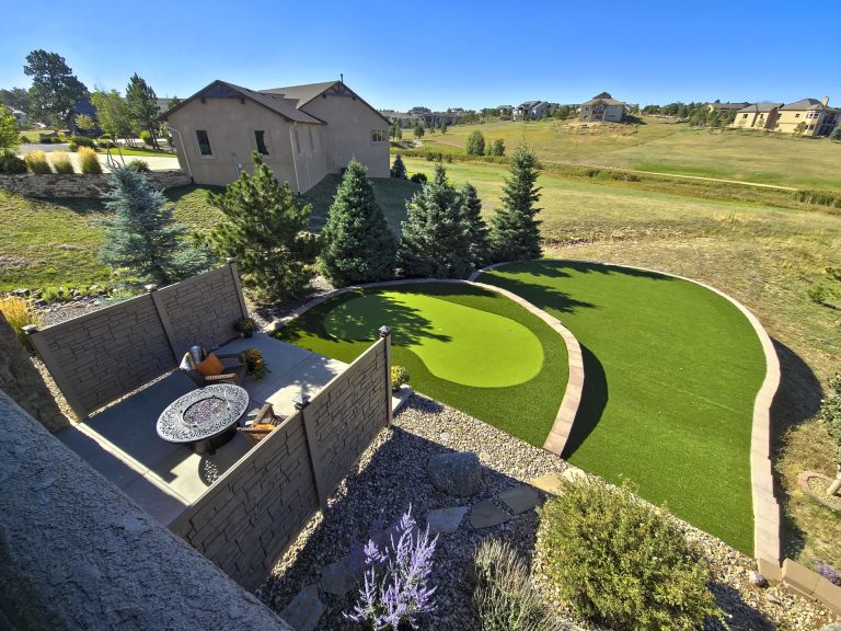Aerial view of a residential property with manicured lawn, curved landscaping, patio area, and surrounding homes in a