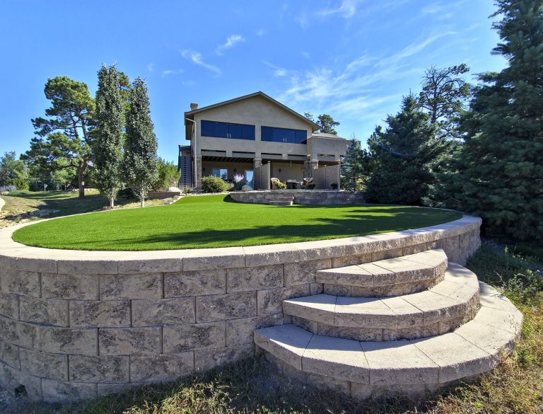 Modern two-story residential home on elevated lot with stone retaining wall and manicured lawn