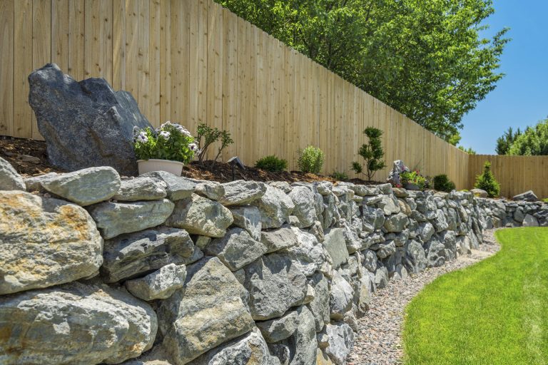 Stone retaining wall with wooden fence and manicured lawn in a residential backyard setting