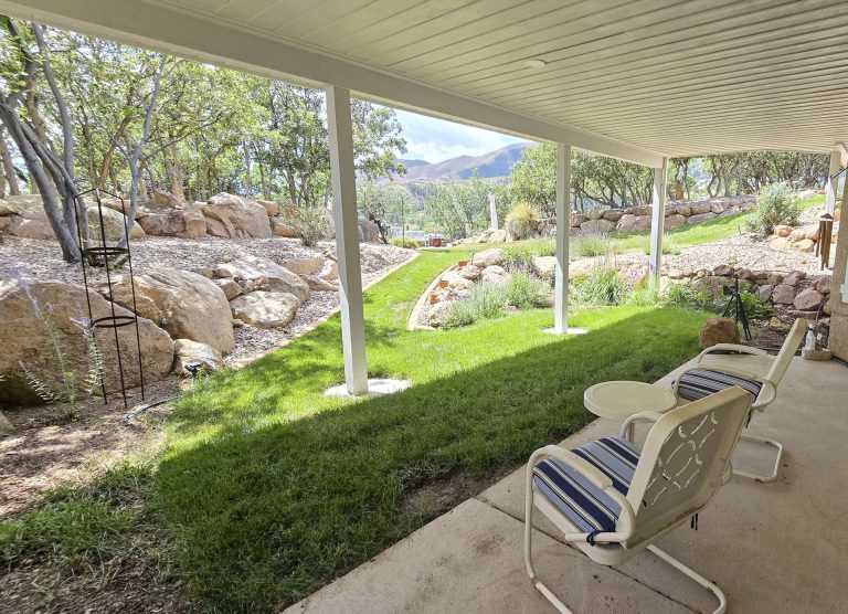 Covered patio with chairs overlooking manicured lawn, trees, and mountains in the distance