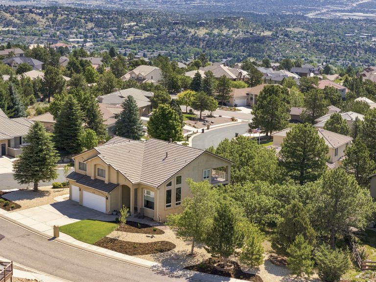 Aerial view of a modern home with a large wooden pergola in a residential neighborhood surrounded by trees