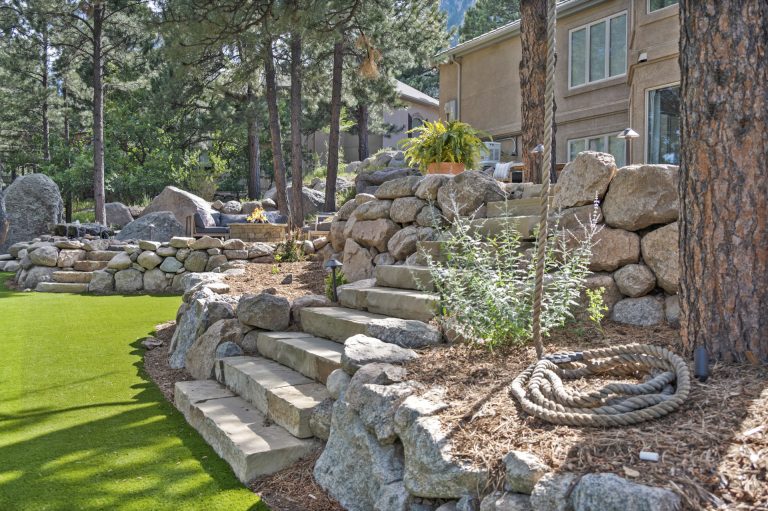 Stone steps and retaining wall in a residential backyard with evergreen trees and manicured lawn
