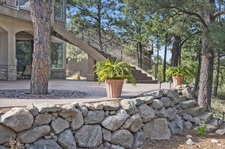 Stone wall border in front of a house with mature trees and exterior staircase