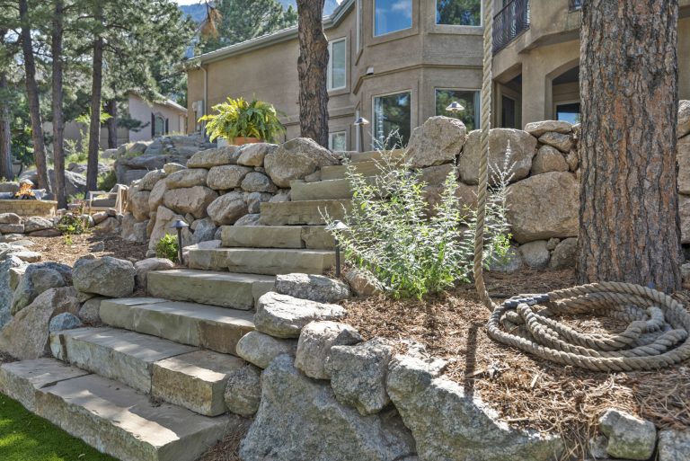 Stacked stone logs and landscaping rocks near trees outside a brick building