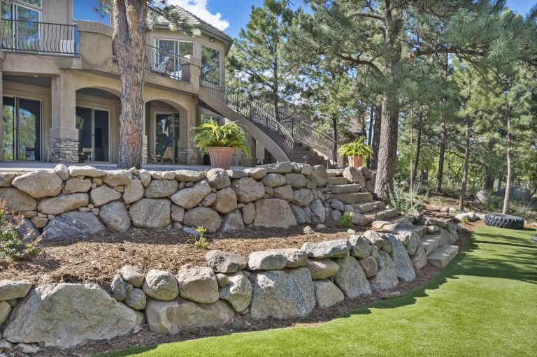 Stone retaining wall in curved formation with manicured lawn and residential home in background
