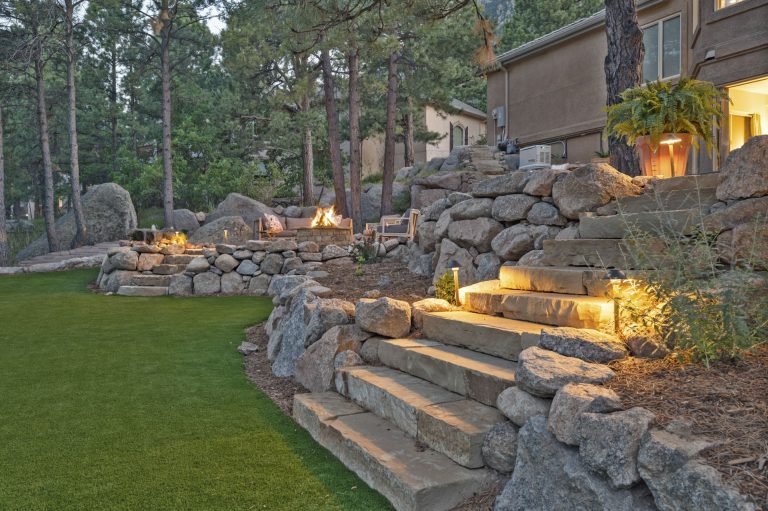 Illuminated stone retaining wall and steps in a landscaped residential backyard at dusk