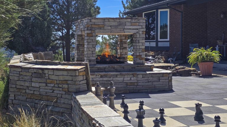 Backyard patio with stone walls, chessboard, seating areas, and brick house with landscaping