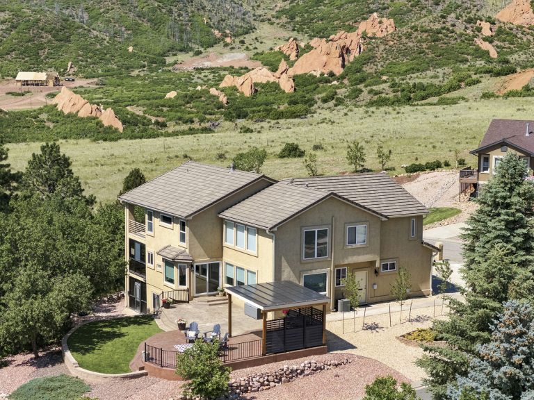 Modern two-story home with stone patio and pergola surrounded by landscaping on hillside terrain