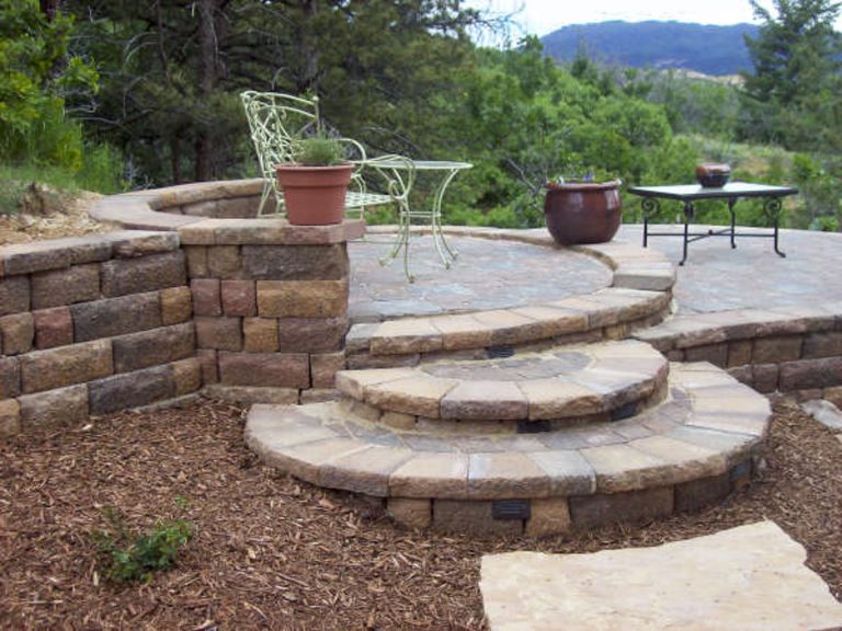 Backyard patio area with curved stone seating walls, fire pit, metal furniture, and mountain view in background