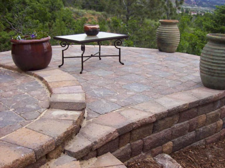 Elevated patio with stone pavers, seating furniture, and decorative planters overlooking a hillside landscape