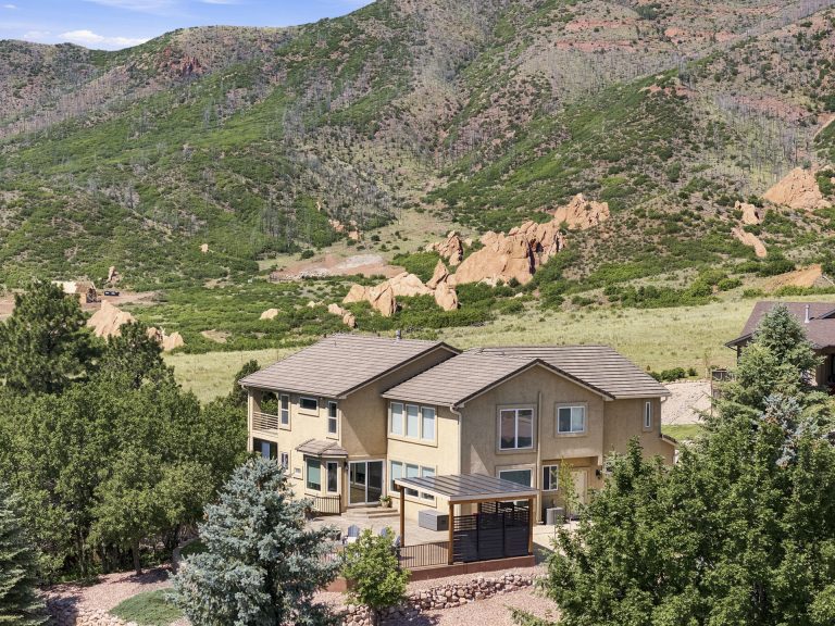 Two-story brown house with deck overlooking green valley and mountains in Colorado landscape