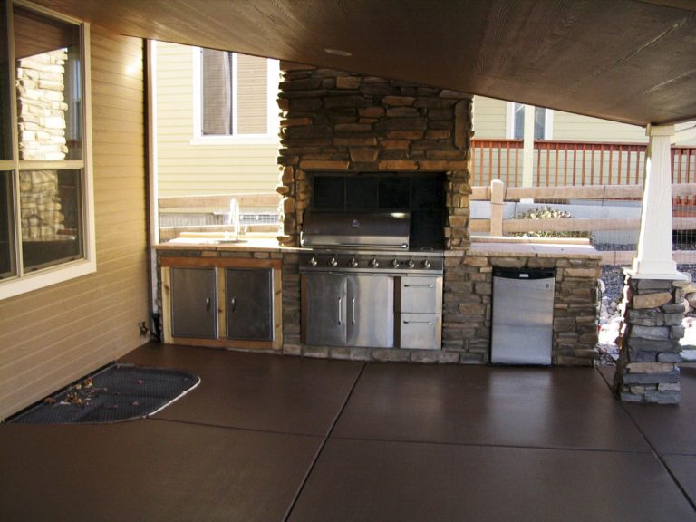 Covered outdoor patio with built-in grill, stone fireplace, stainless steel cabinets, and concrete flooring