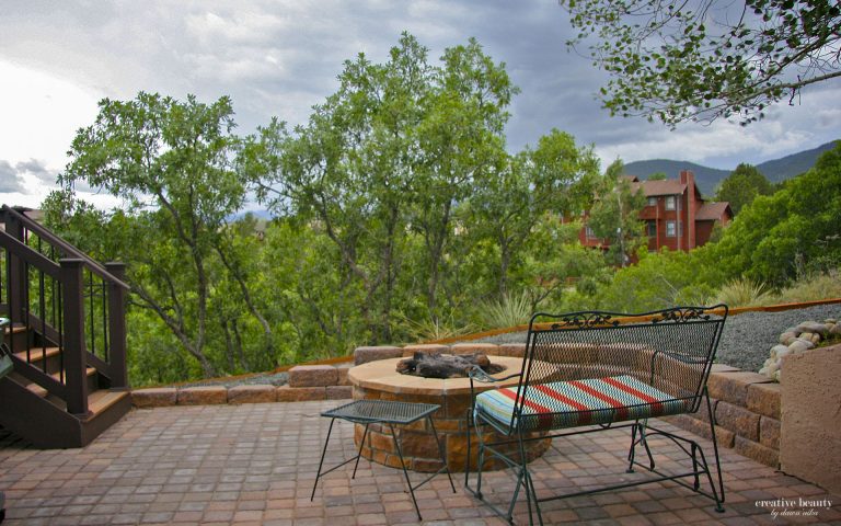 Outdoor patio deck with dining table, chairs, and fire pit overlooking green trees and mountains