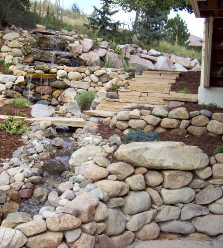 Terraced landscape with stacked boulder retaining walls and wooden steps on a hillside with scattered vegetation